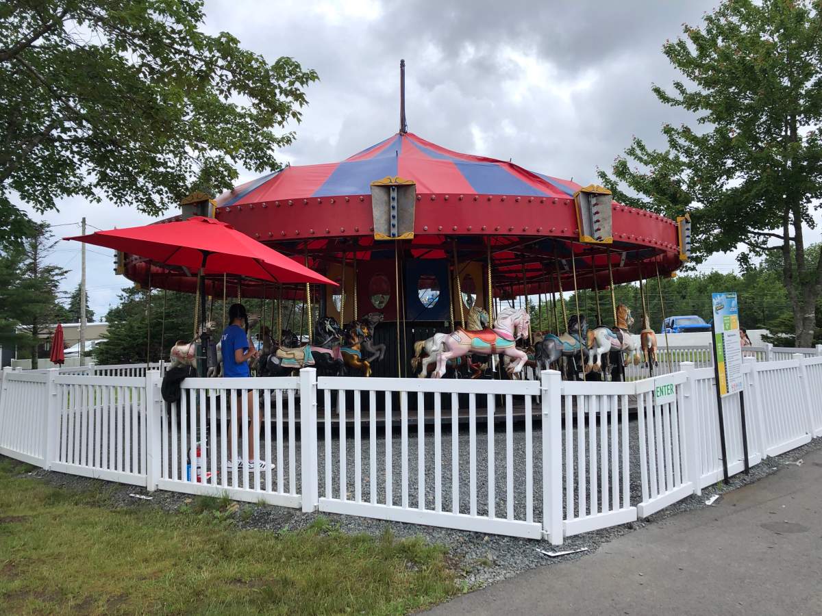 An employee of the theme park stands by an empty carousel on an overcast day.