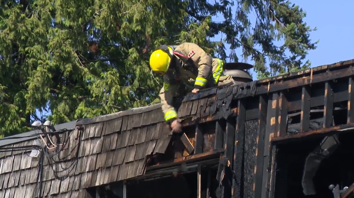 A firefighter knocks pieces off of the roof of a Burnaby, B.C. home after a fire on Sat. July 15, 2023. No one was injured, but several residents were displaced.