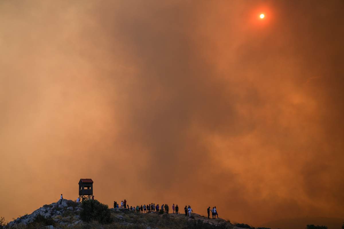 People watch the fire in Mandra west of Athens, on Tuesday, July 18, 2023. In Greece, where a second heatwave is expected to hit Thursday, three large wildfires burned outside Athens for a second day. Thousands of people evacuated from coastal areas south of the capital returned to their homes Tuesday when a fire finally receded after they spent the night on beaches, hotels and public facilities. (AP Photo/Petros Giannakouris)
