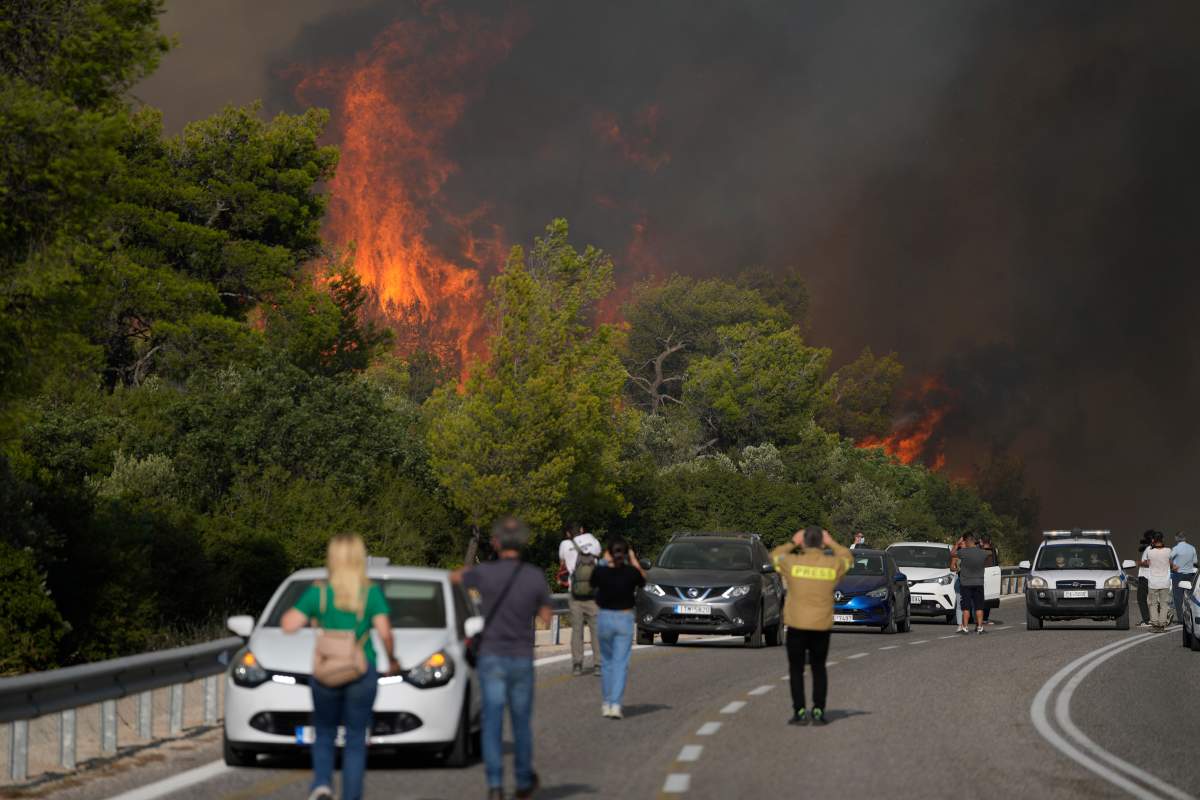 A fire burns trees next of a road with people and vehicles at the village of Agia Sotira near Athens, on Tuesday, July 18, 2023. In Greece, where a second heatwave is expected to hit Thursday, three large wildfires burned outside Athens for a second day. Thousands of people evacuated from coastal areas south of the capital returned to their homes Tuesday when a fire finally receded after they spent the night on beaches, hotels and public facilities. (AP Photo/Thanassis Stavrakis)