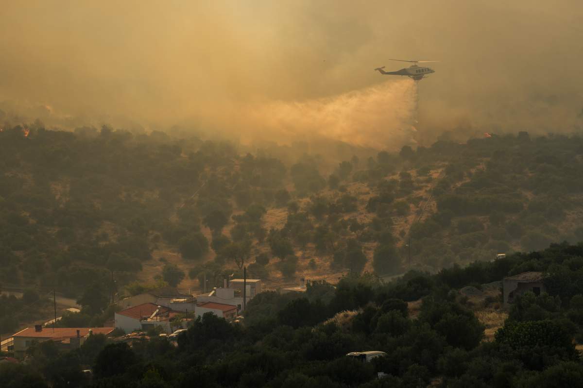 A firefighting helicopter dumps water in Mandra west of Athens, on Tuesday, July 18, 2023. In Greece, where a second heatwave is expected to hit Thursday, three large wildfires burned outside Athens for a second day. Thousands of people evacuated from coastal areas south of the capital returned to their homes Tuesday when a fire finally receded after they spent the night on beaches, hotels and public facilities. (AP Photo/Petros Giannakouris)