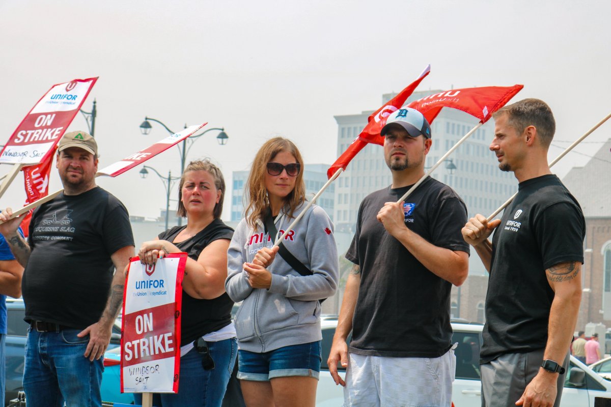 Five people stand with flags and signs as part of a strike involving Windsor Salt workers in Windsor, Ont.