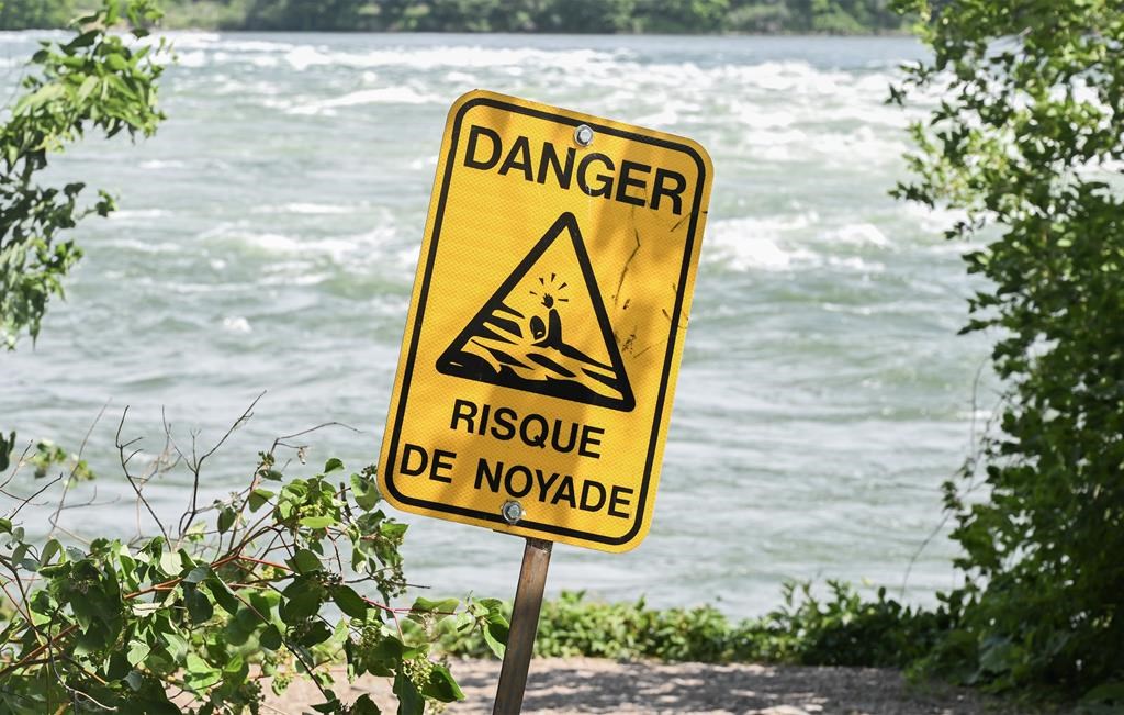 A sign that translates to "risk of drowning," is shown next to the St. Lawrence River in Montreal on Monday, June 26, 2023. 