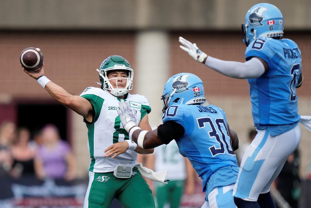 Saskatchewan Roughriders quarterback Mason Fine, left, throws under pressure from Toronto Argonauts' Jonathan Jones, centre, and Adarius Pickett during the first half of CFL action in Halifax on Saturday, July 29, 2023. THE CANADIAN PRESS/Darren Calabrese.