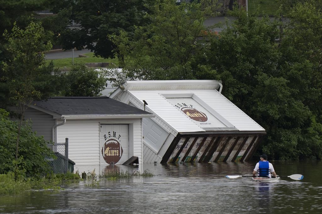 Buildings are seen upended on a riverbank as a man paddles a kayak through floodwater following a major rain event in Halifax on Saturday, July 22, 2023. THE CANADIAN PRESS/Darren Calabrese.
