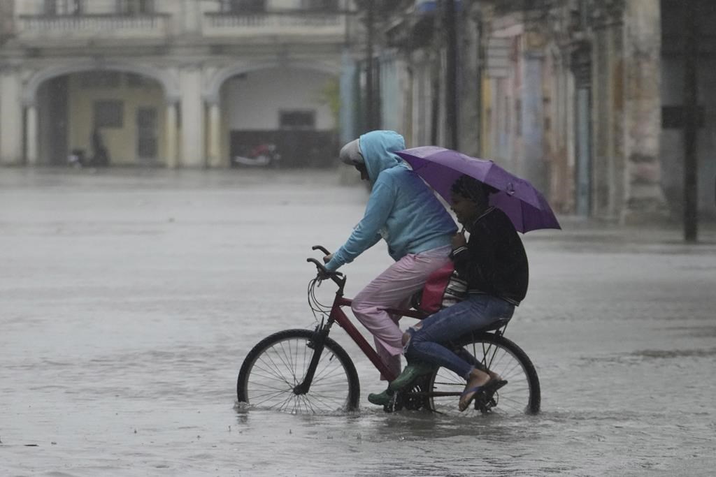 Commuters cycle through a street flooded by rain brought by Hurricane Idalia in Havana, Cuba, early Tuesday, Aug. 29, 2023. (AP Photo/Ramon Espinosa)