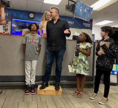 Anchor Scott Roberts giving himself a little boost while being measured by our 2023 reporters for the day — Aaryan, Olivia, Cecily and Hudson —in the Global Edmonton newsroom on Wednesday, August 23, 2023.