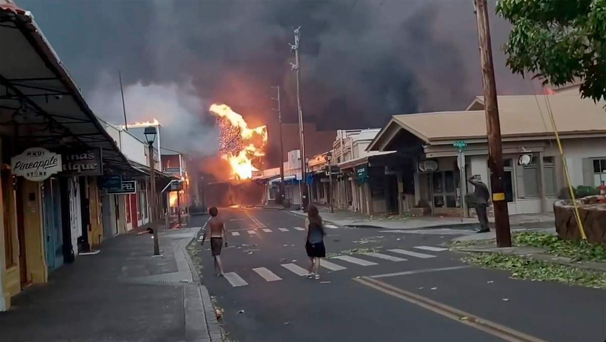 People watch as smoke and flames fill the air from raging wildfires on Front Street in downtown Lahaina, Maui on Tuesday, Aug. 9, 2023. Maui officials say wildfire in the historic town has burned parts of one of the most popular tourist areas in Hawaii.