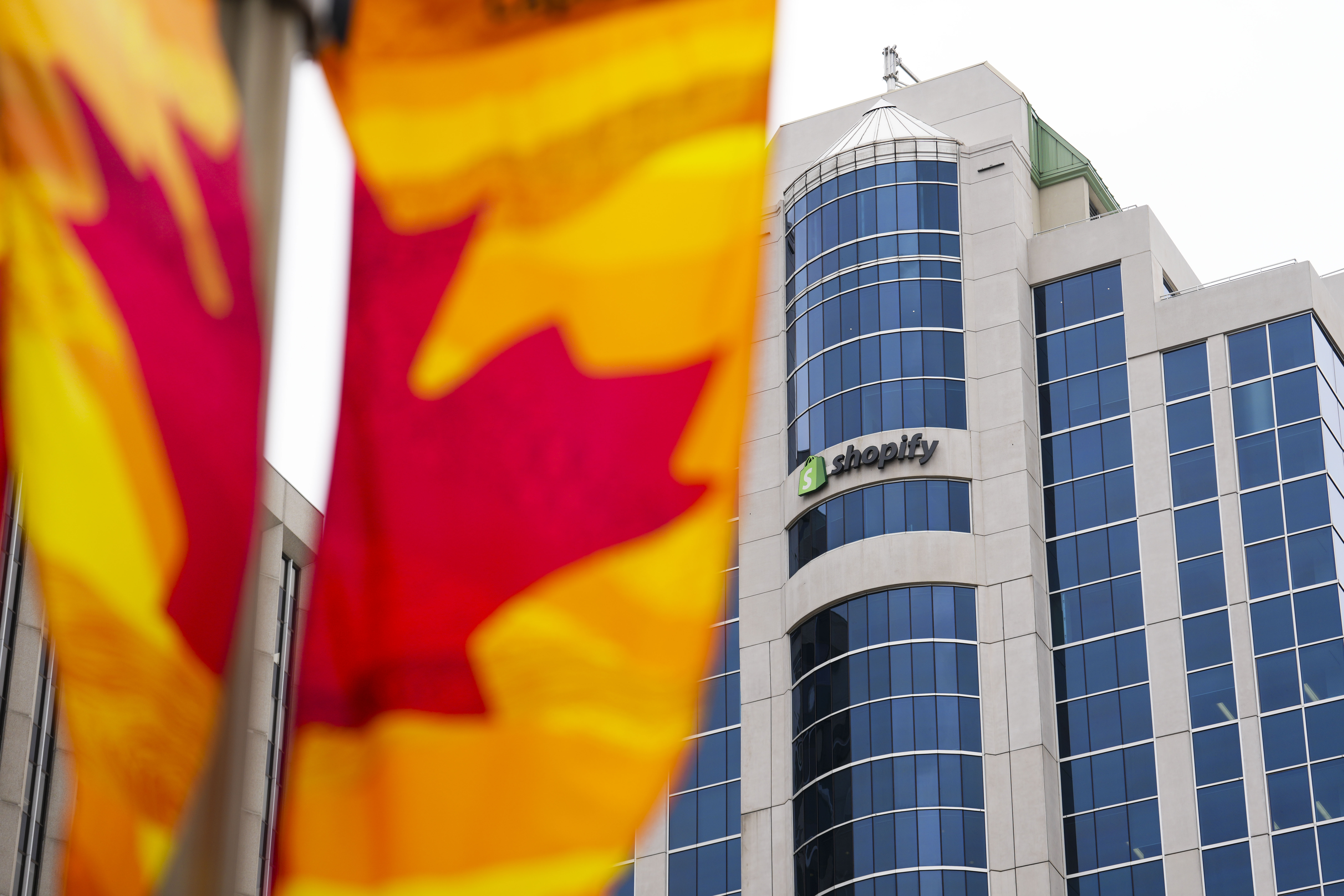 The shopify office is seen in the background of a maple leaf flag.
