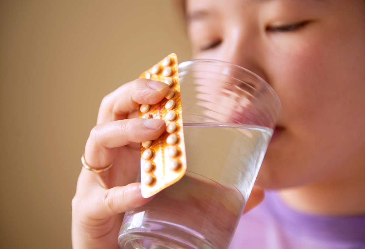 A woman holds a glass of water and an unlabeled package of birth control pills.