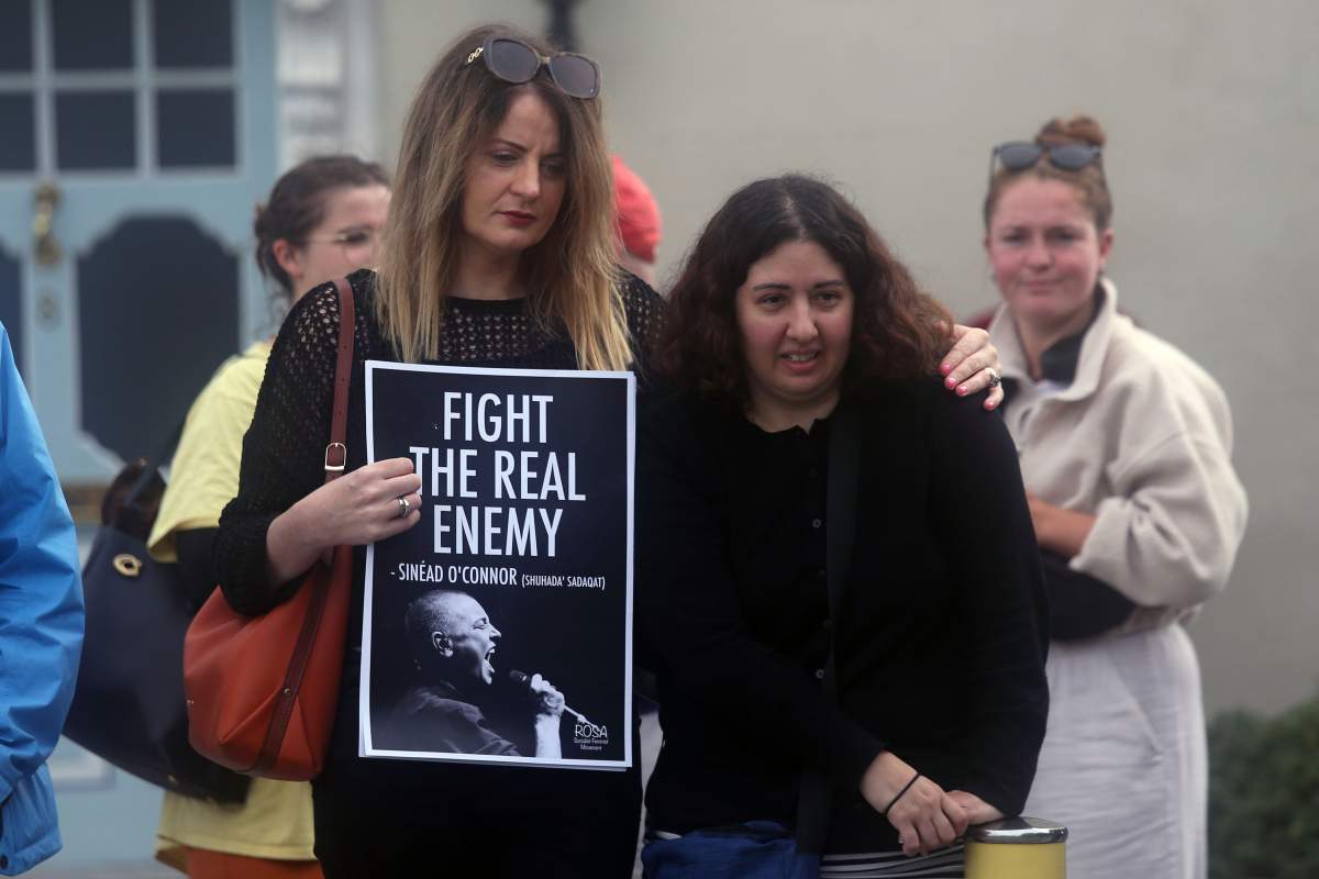 A woman holds a poster with O'Connor's photo. The poster reads "Fight the real enemy."