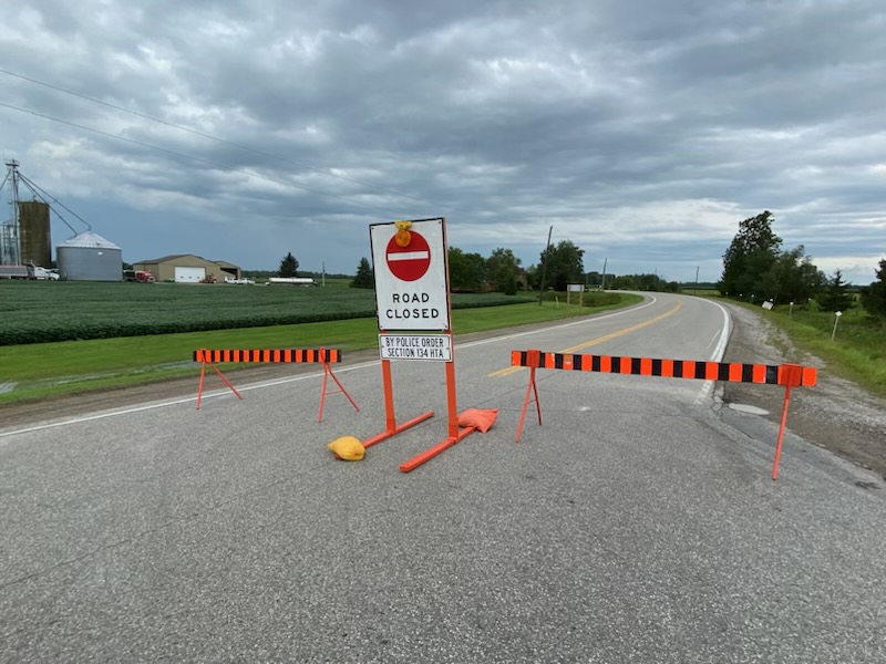 A section of road blocked by a road closed sign with dark clouds above.