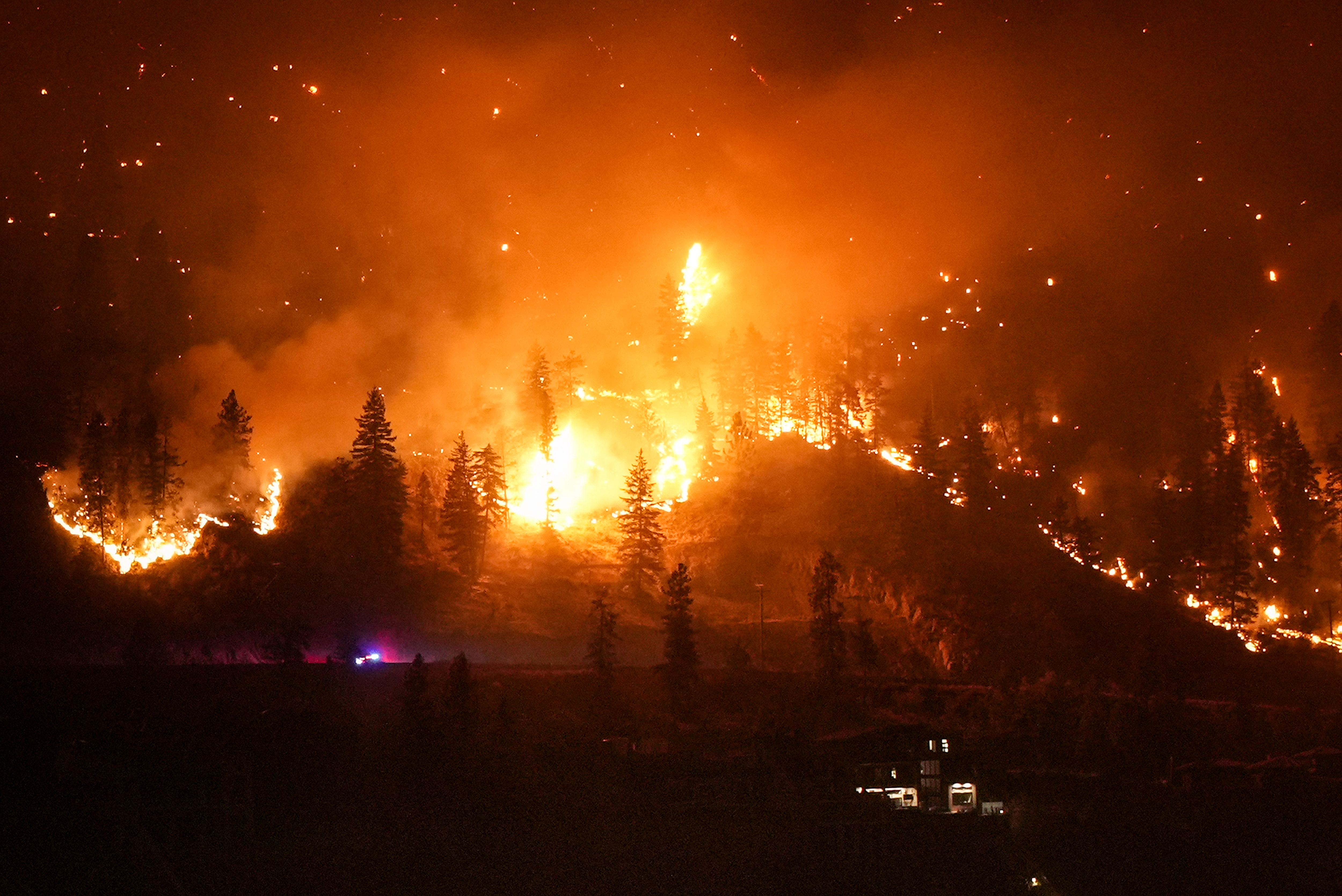 The McDougall Creek wildfire burns on the mountainside above a lakefront home.