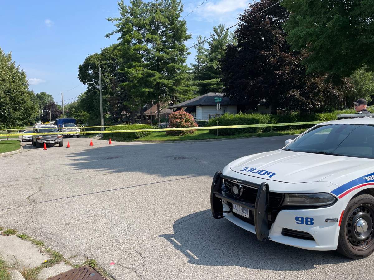 The front of a London police cruiser and caution tape blocking off a residential street on a sunny day.