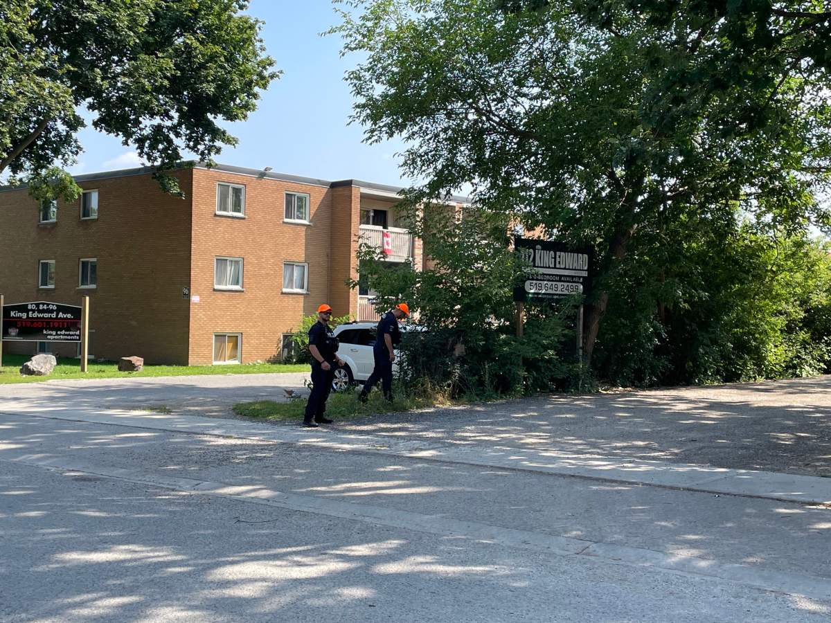 A brown brick building with two men walking in front of it on a sunny summer day.