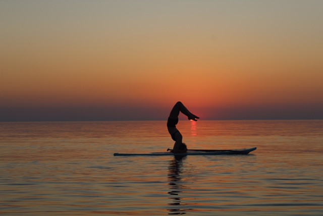 The silhouette of someone doing yoga on a standup paddleboard on the lake during sunset.