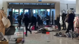 A group of people dressed in black hoodies are seen robbing a department store. There is merchandise on the ground.