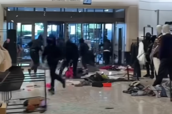 A group of people dressed in black hoodies are seen robbing a department store. There is merchandise on the ground.