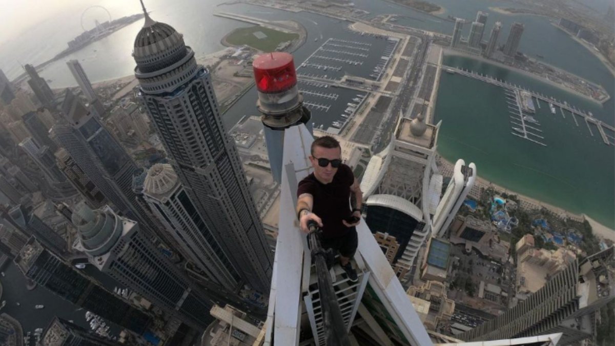 Remi Lucidi standing on a skyscraper. He is using a selfie stick to take the photo. The ground is far below.