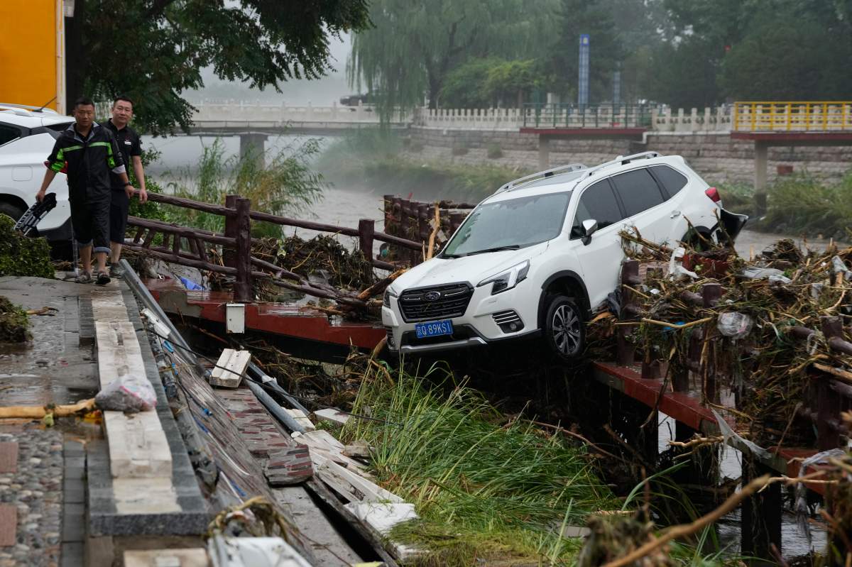 Residents walk near a vehicle washed away by flood waters in the Mentougou district on the outskirts of Beijing, Tuesday, Aug. 1, 2023.