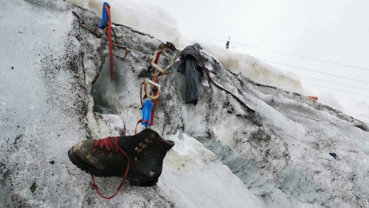 A brown hiking boot laying in the snow next to rusted climbing gear.