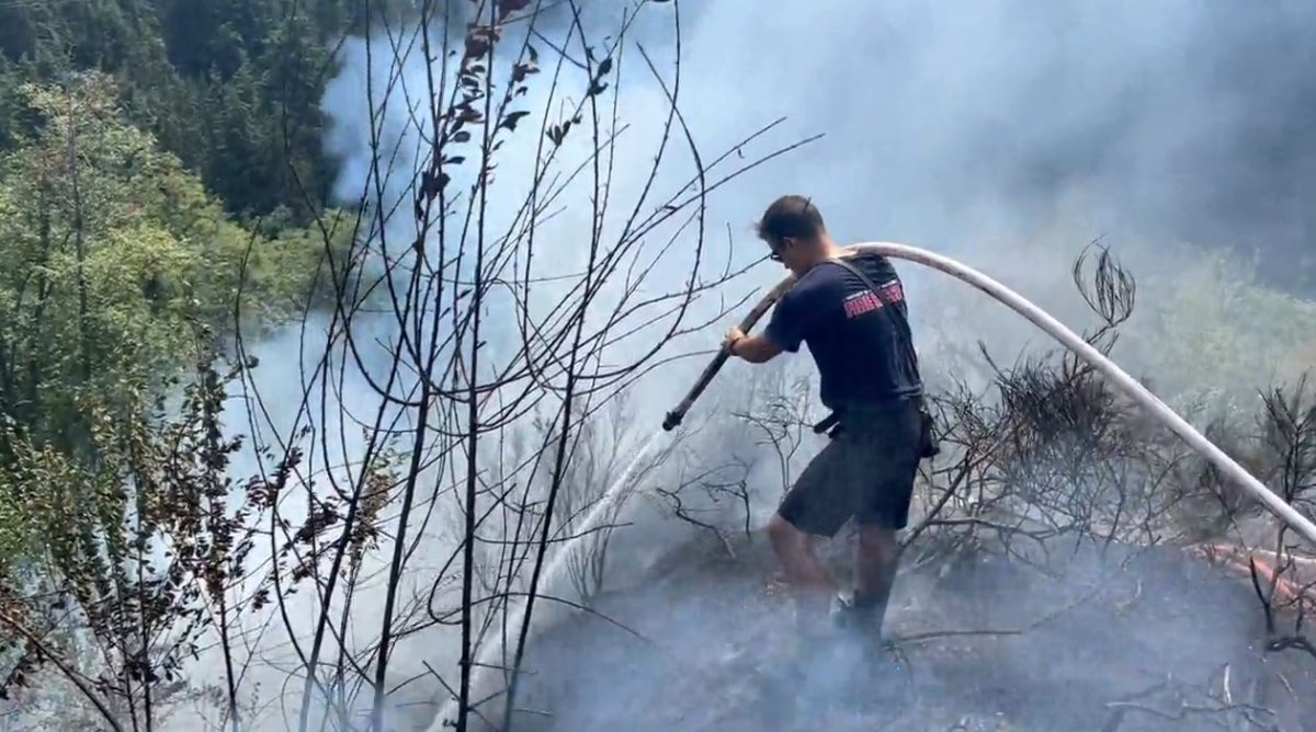 A firefighter douses hot spots from a brush fire on Grouse Mountain on Monday, Aug. 7, 2023.