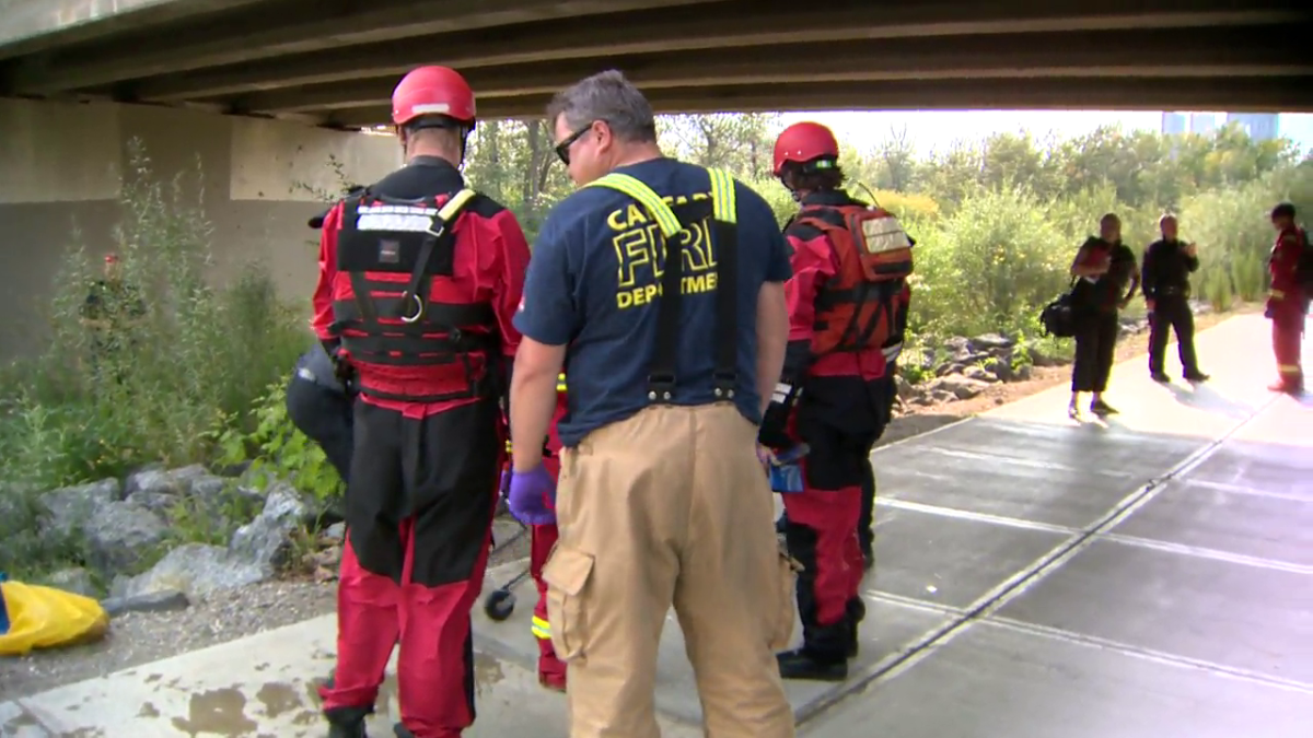 Members of the Calgary Fire Department's aquatic rescue team look on as other emergency responders load a body on a stretcher that they helped recover from the Bow River on Aug. 4, 2023. Police said they're not sure if the death is suspicious.
