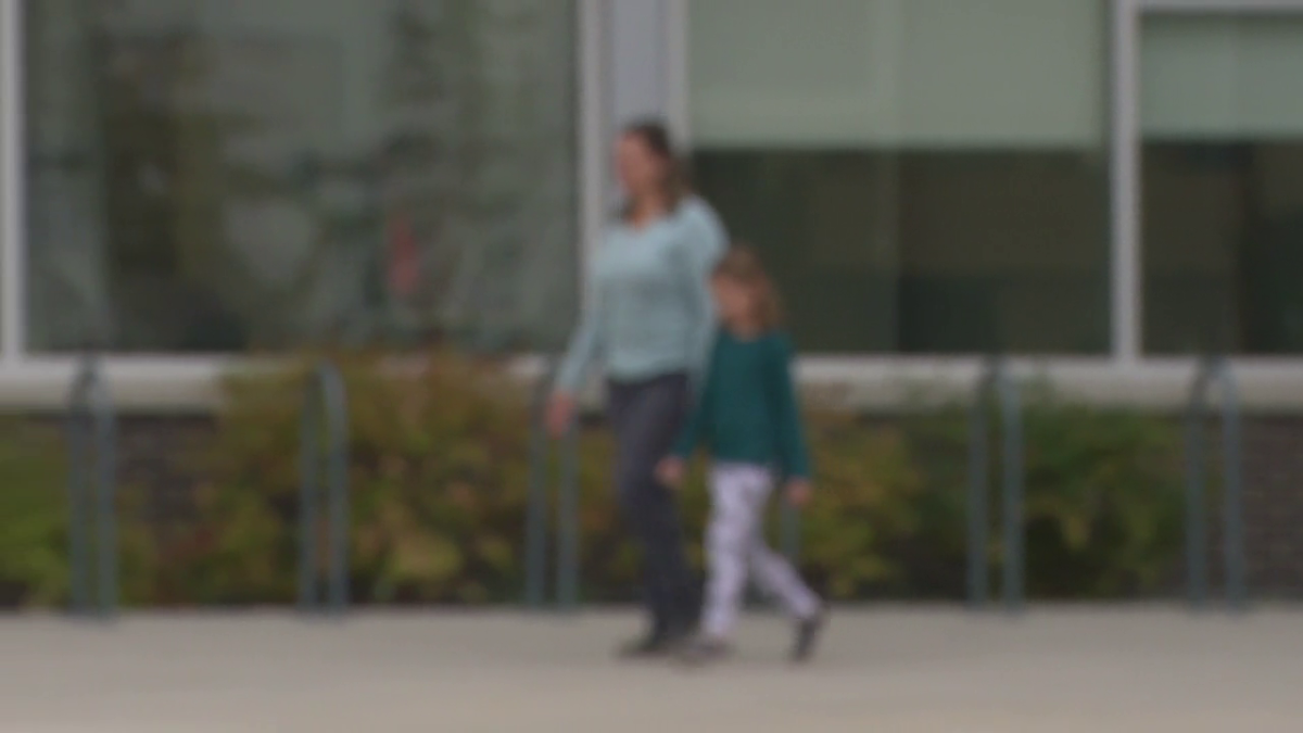 An adult and child walk in front of a Calgary school on Aug. 30, 2023.