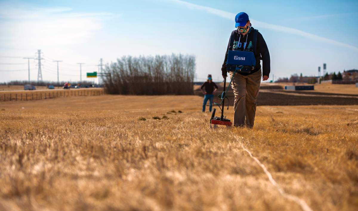 A woman walks through a field carrying a machine