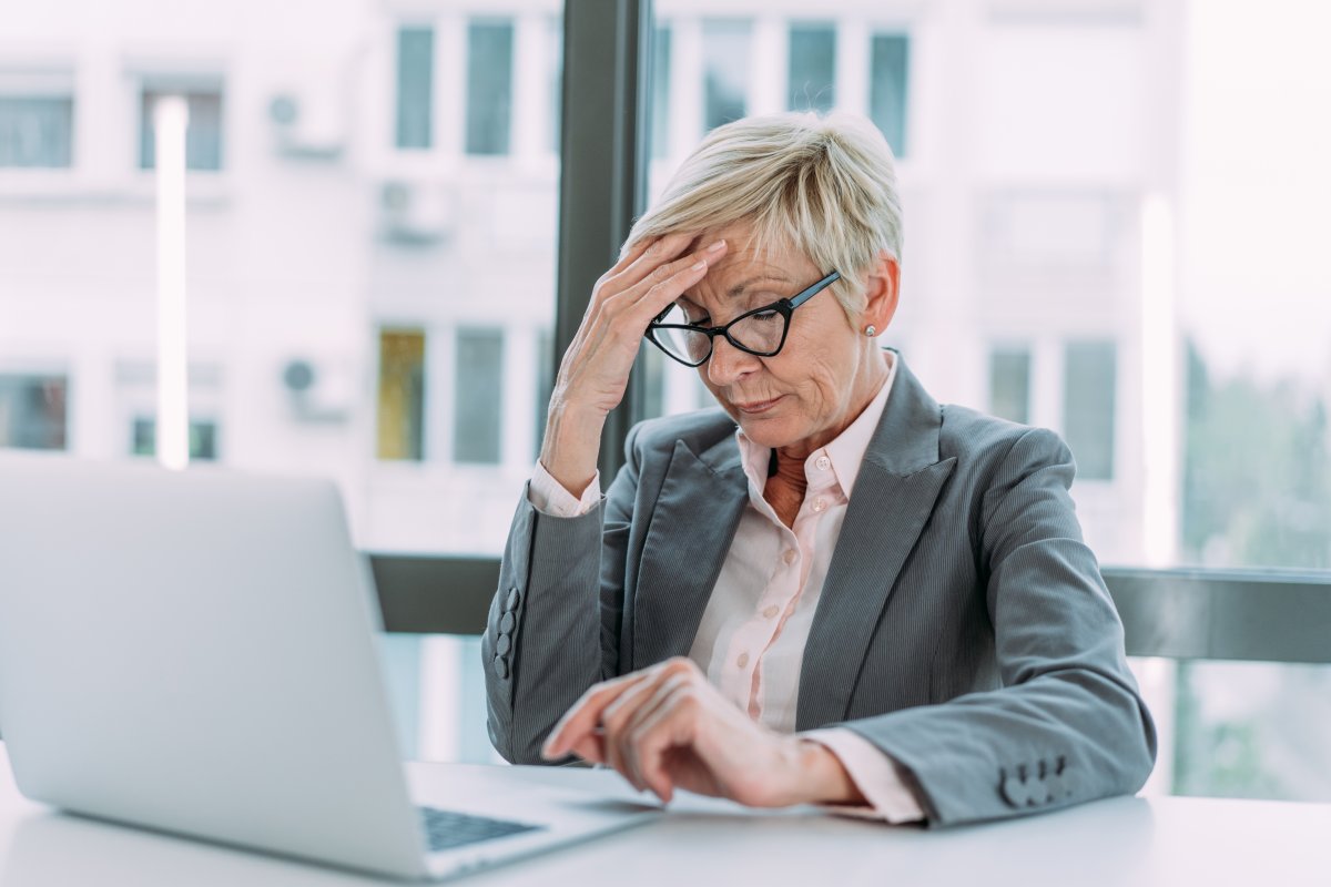 Shot of stressed businesswoman sitting at her desk and holding head with hand. Overworked businesswoman sitting in front of laptop and holding head.
