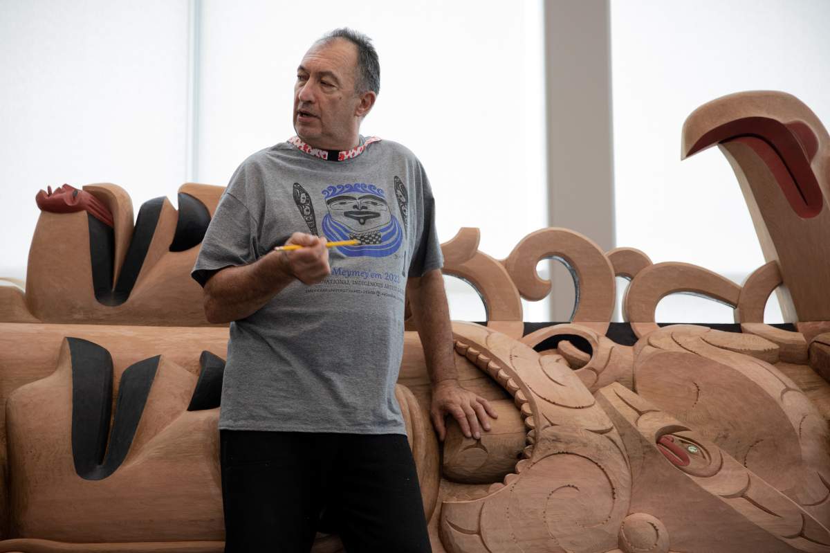A man stands leaning on a totem pole.
