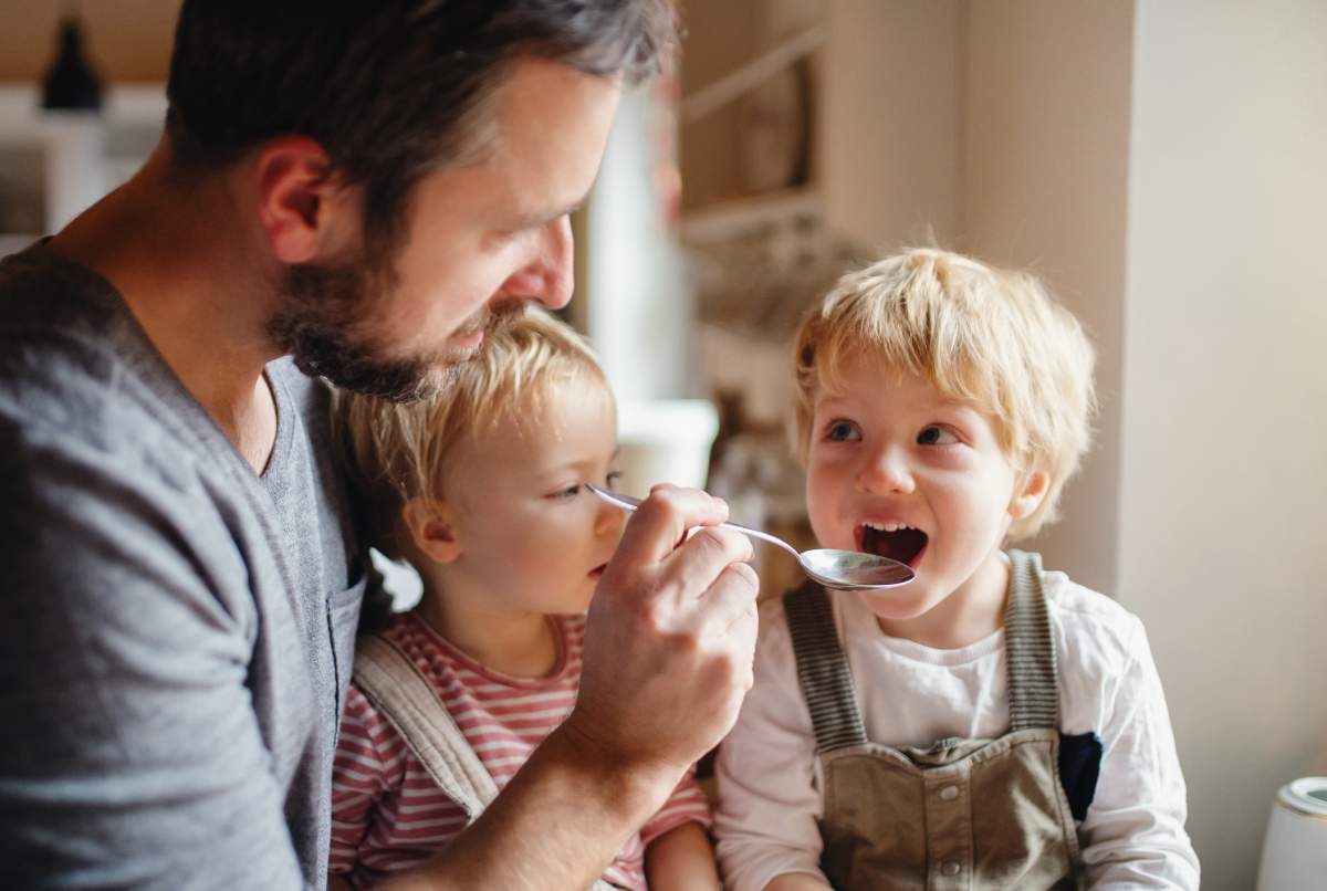 A father on paternity leave looking after two children indoors.