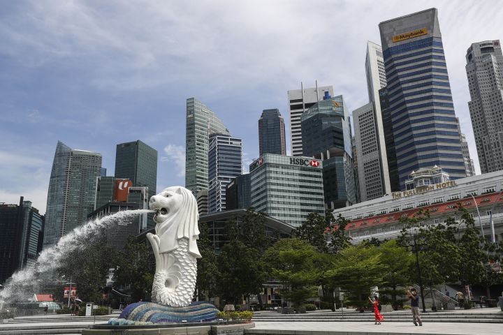 FILE - People are dwarfed against the financial skyline as they take photos of the Merlion statue along the Marina Bay area in Singapore, Tuesday, June 30, 2020.