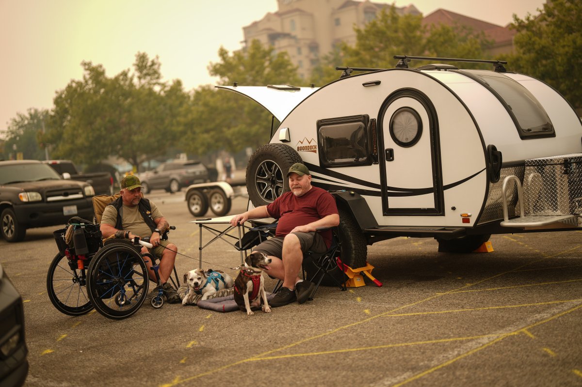 Veteran Rob Pullen, left, and Warren Pullen, who were evacuated from their home on Thursday due to wildfires, sit with their dogs outside their trailer in the parking lot at an evacuation centre, in Kelowna, B.C., on Aug. 19.