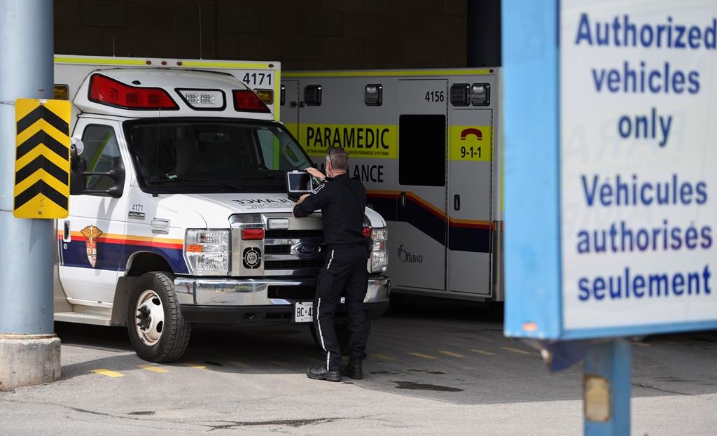 A paramedic works on a laptop on the hood of their ambulance, outside the Emergency Department at the Ottawa Hospital Civic Campus in Ottawa on Monday, May 16, 2022. Ottawa paramedics are seeking provincial approval for a new program that would see some patients with non-urgent concerns taken to hospital in a taxi, in a bid to ease the crushing demands on ambulance crews. THE CANADIAN PRESS/Justin Tang.