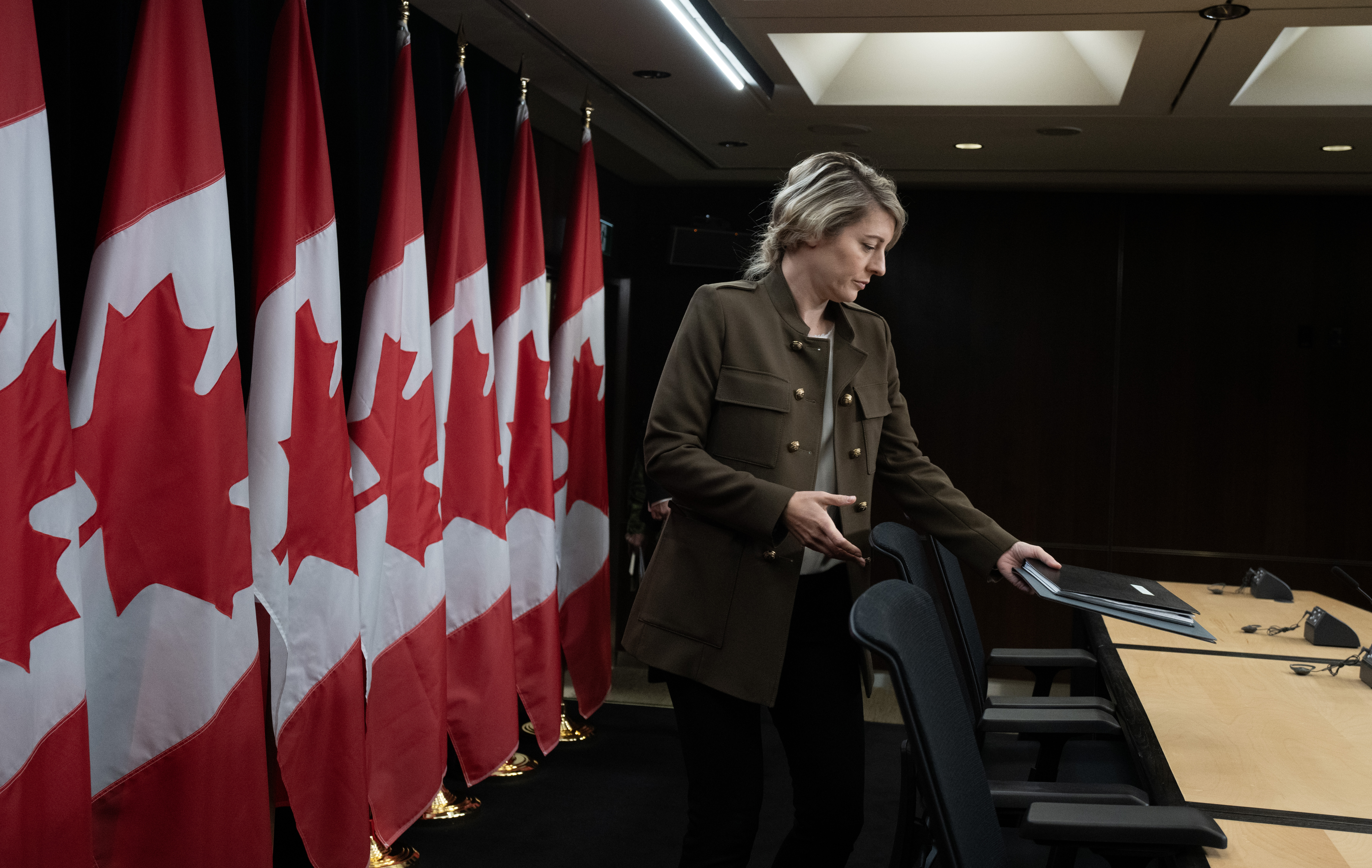 Minister of Foreign Affairs Melanie Joly takes her seat as she arrives for a news conference, with a row of Canadian flags behind her.