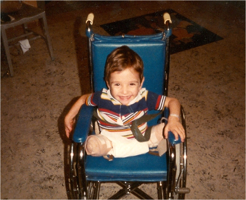 Spencer West as a young boy in a wheelchair, smiling to camera