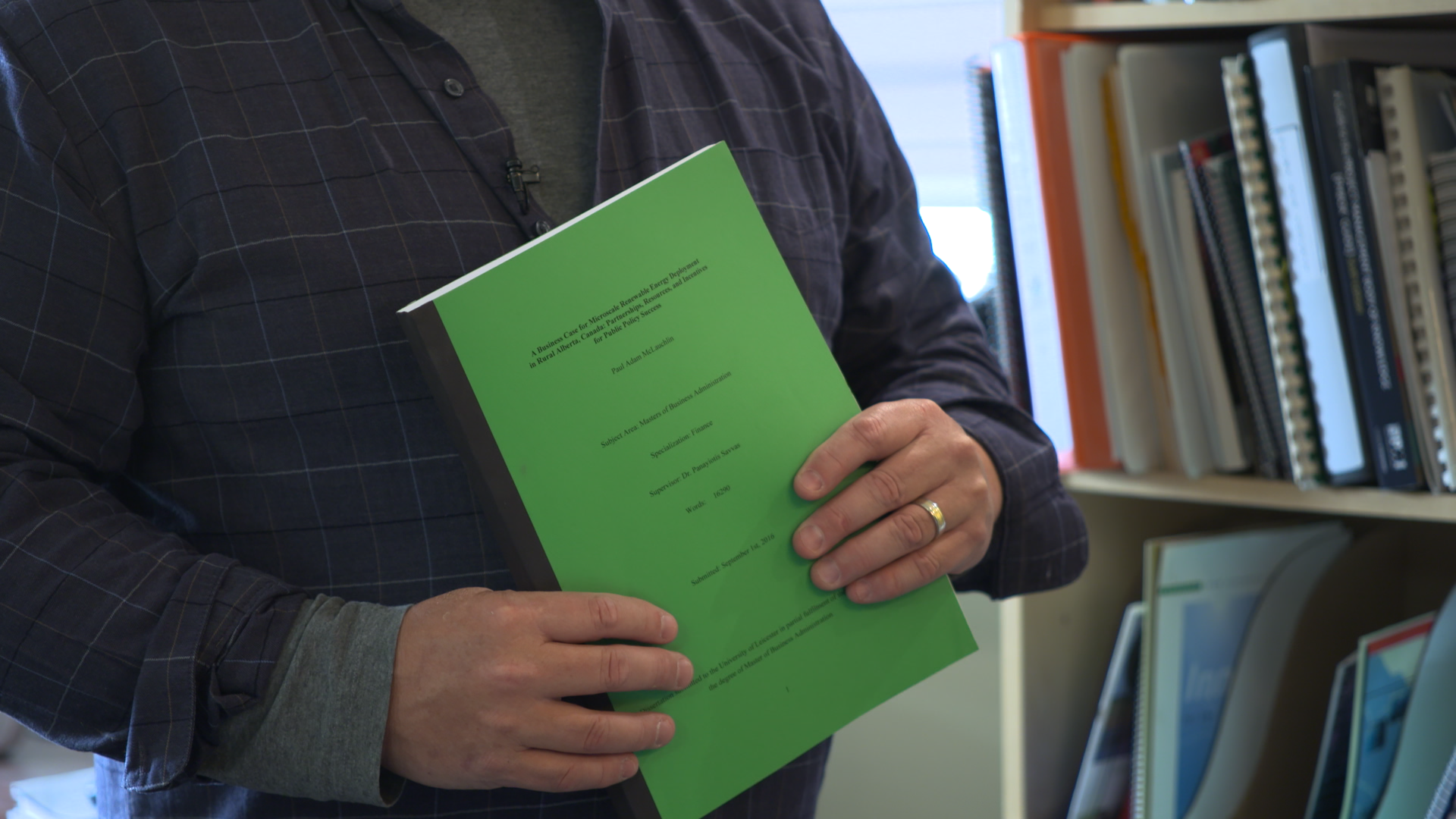 Paul McLauchlin holds up his 2015 master’s thesis on micro-renewable energy generation opportunities in rural Alberta.