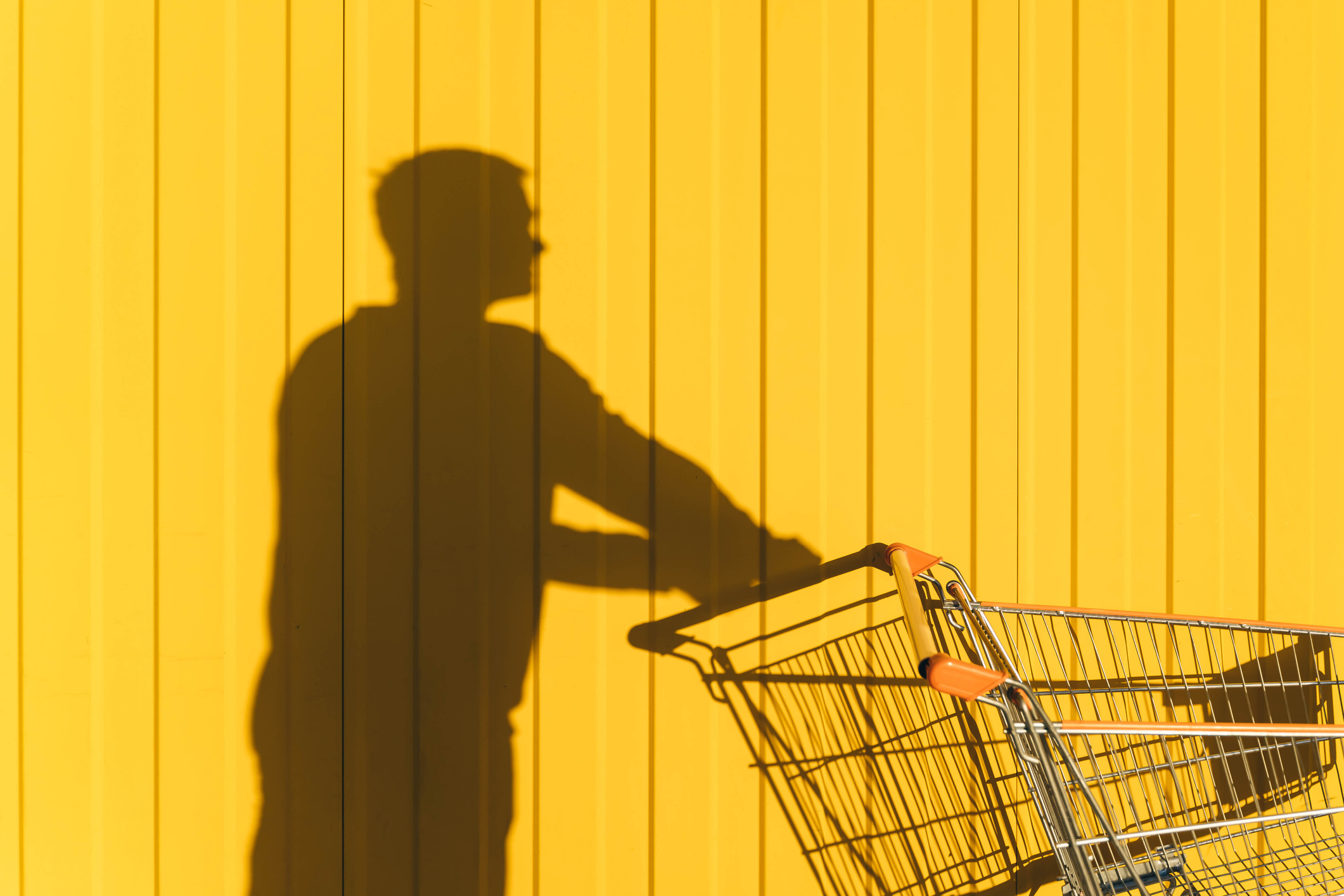 Young man shadow and shopping cart on Yellow background. Shopping concept.
