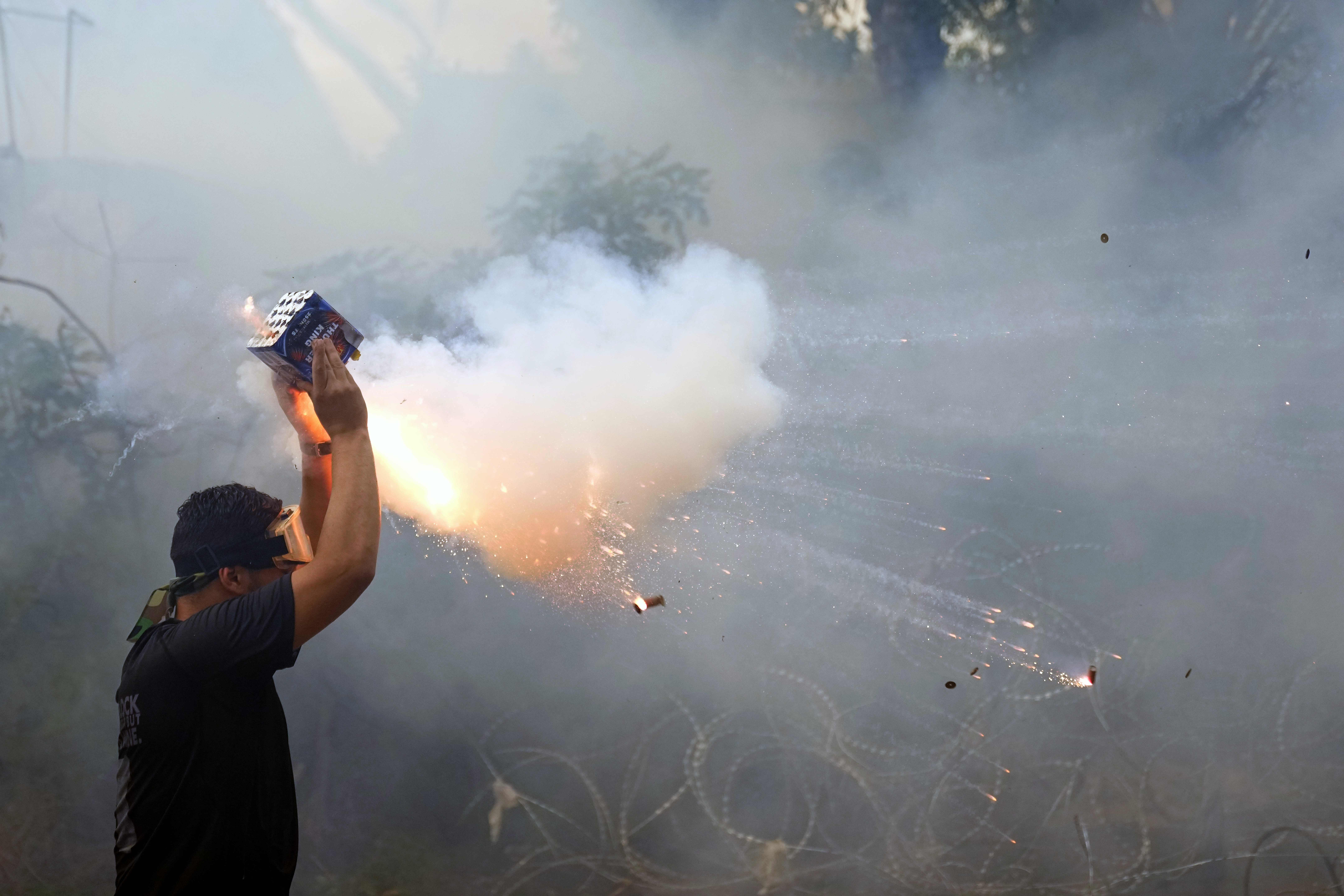 A protester launches fireworks at riot police.