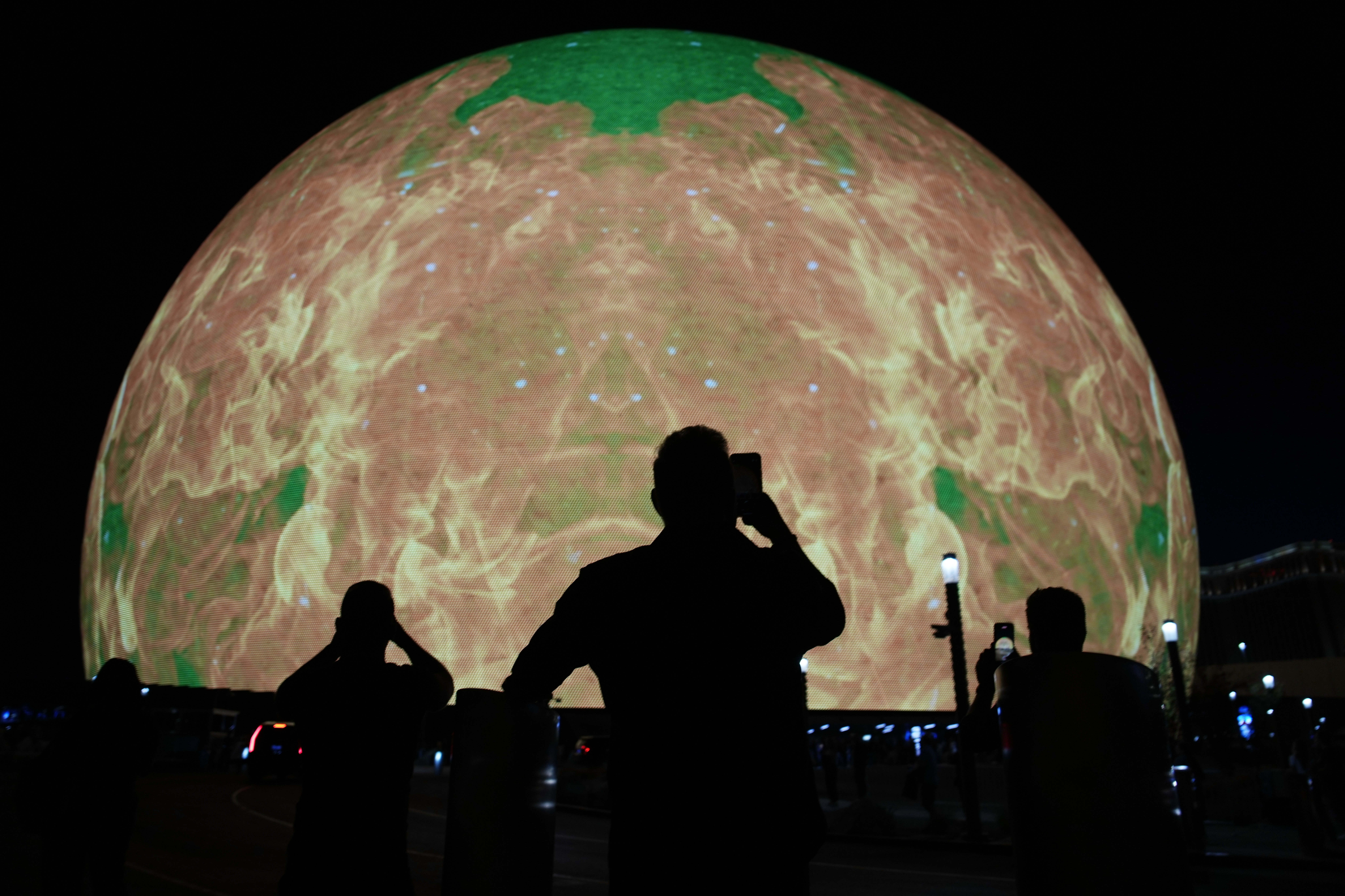 The Sphere, a visual display, rises in a massive curve in front of a silhouetted person in Las Vegas.
