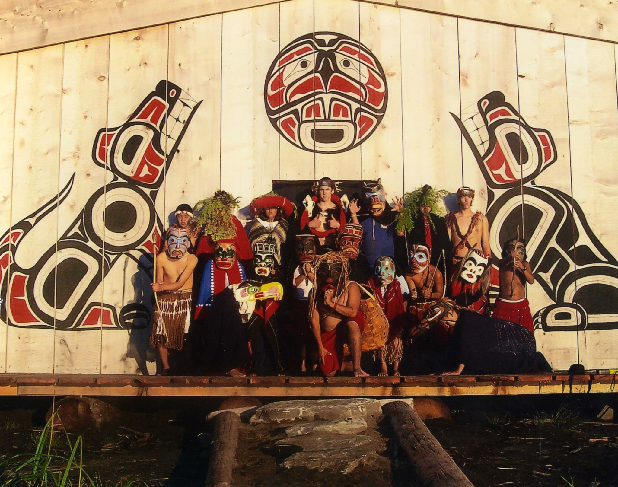 A group of people stand in front of a big house with west coast art marking the fron