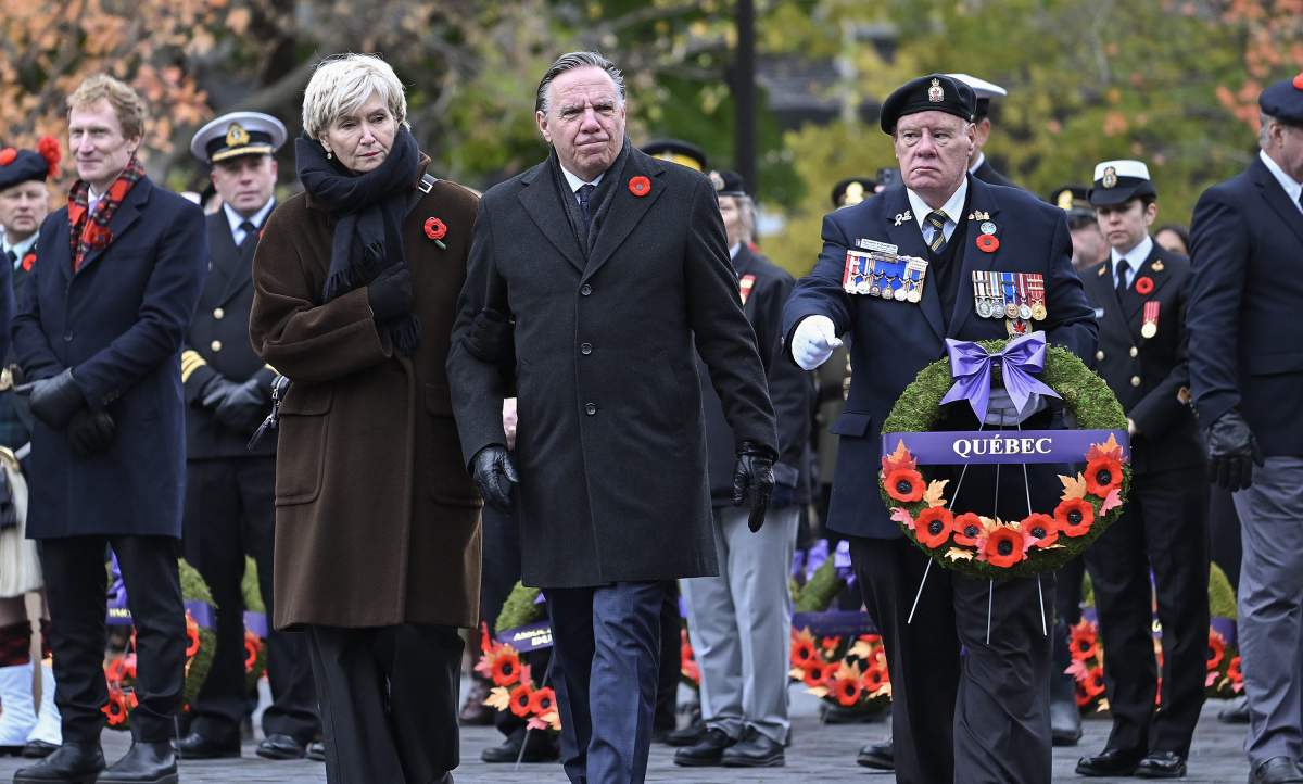 Quebec Premier Francois Legault, centre, lays a wreath alongside his wife Isabelle Brais and veteran Kenneth Ouellet during a Remembrance Day ceremony in Montreal, Saturday, November 11, 2023.