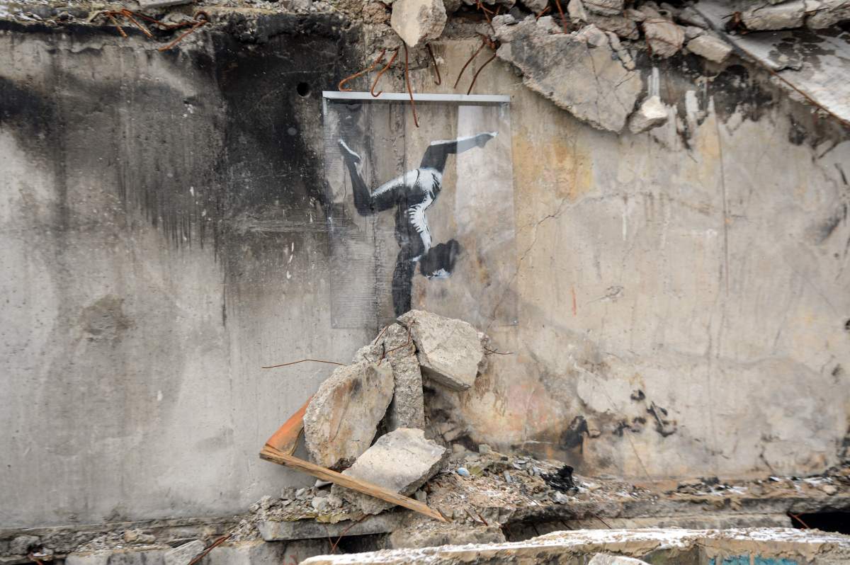 A spraypainted gymnast balances on rubble.