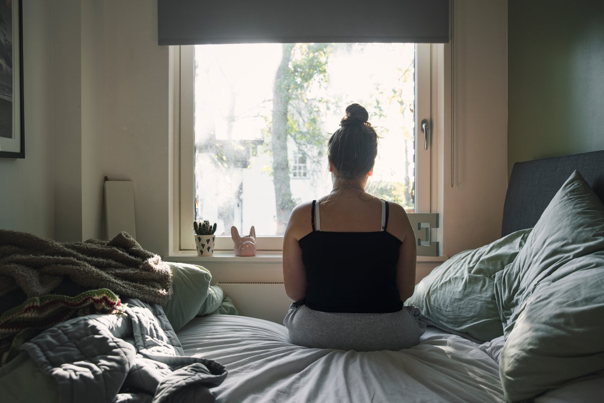 Rear view of a teenage girl looking out of the window whilst sitting on her bed