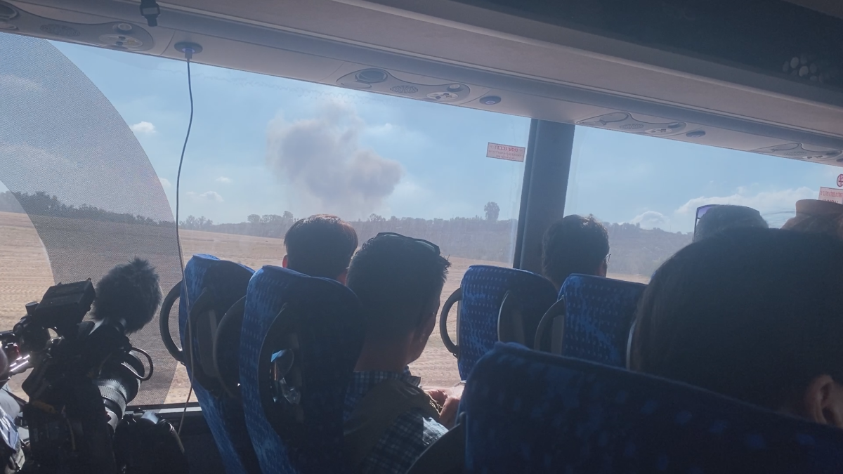 Journalists look out of a bus window at a plume of smoke from Gaza