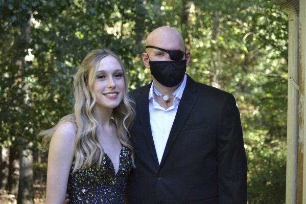 Aaron James and his daughter Allie. James is wearing an eyepatch and a mask over his face. Both James and Allie are in formalwear.