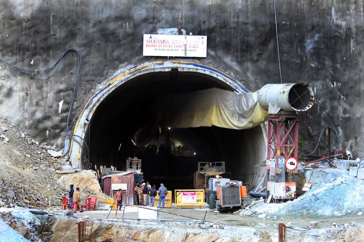 People stand near the entrance to the site of an under-construction road tunnel that collapsed in mountainous Uttarakhand state, India, Friday, Nov. 17, 2023. Rescuers drilled deeper into the rubble of a collapsed road tunnel in northern India on Friday to fix wide pipes for 40 workers trapped underground for a sixth day to crawl to their freedom. (AP Photo)