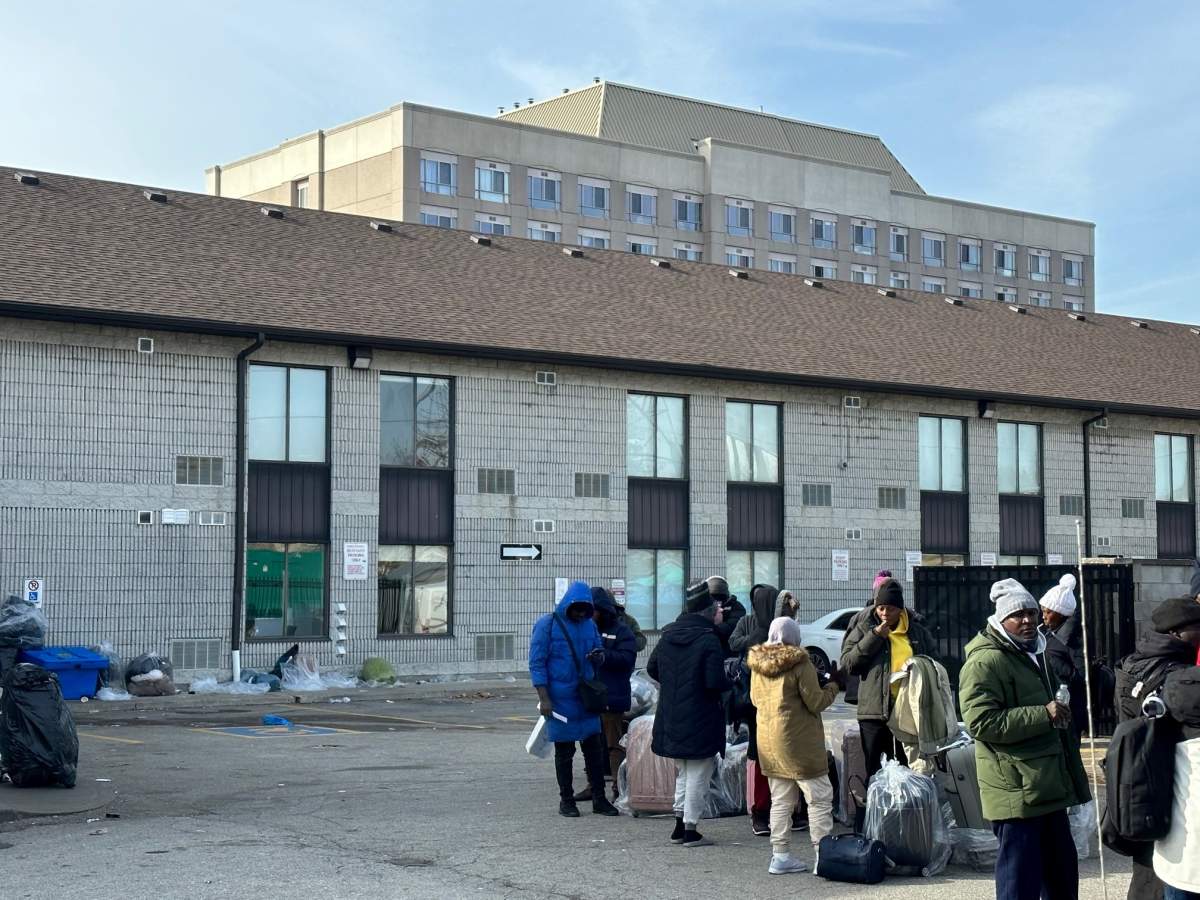 People stand outside of a shelter in Mississauga waiting with suitcases and belongings on Nov. 16, 2023.