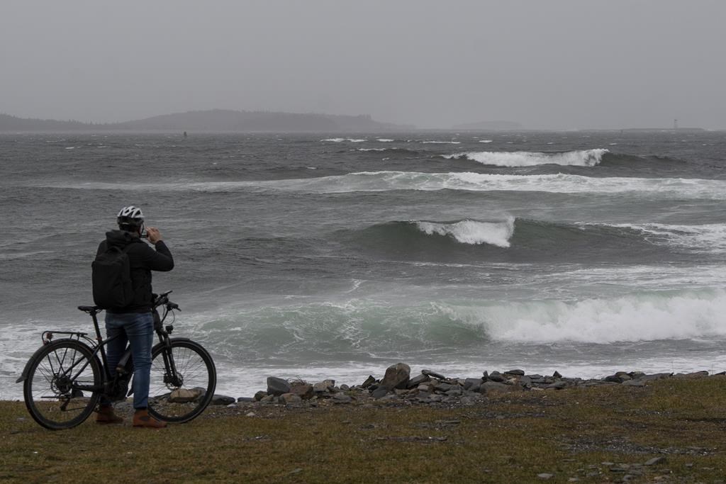 A cyclist photographs waves crashing near Point Pleasant Park in Halifax on Monday, December 18, 2023. Heavy rain and winds gusting over 100km/h knocked out power across the Maritimes. THE CANADIAN PRESS/Darren Calabrese.